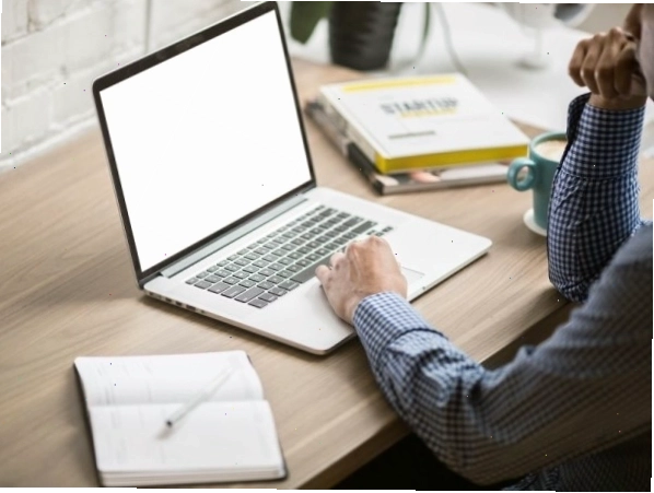 Người đàn ông sử dụng laptop bên cạnh sổ ghi chép và cốc cà phê